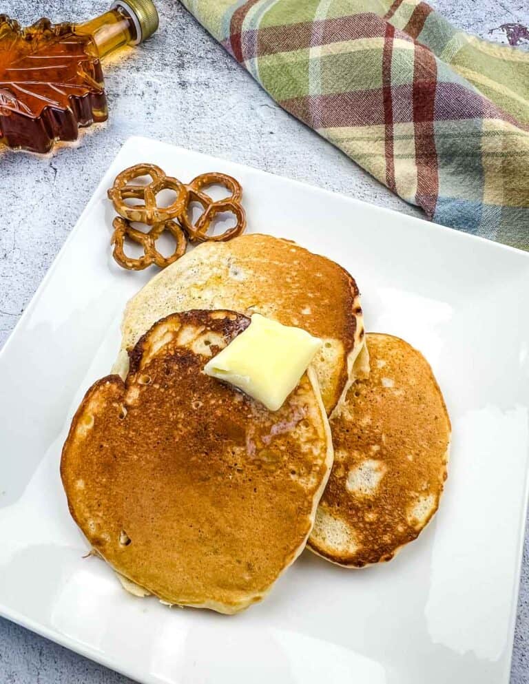 Pretzel pancakes on a plate with butter and syrup in the background.
