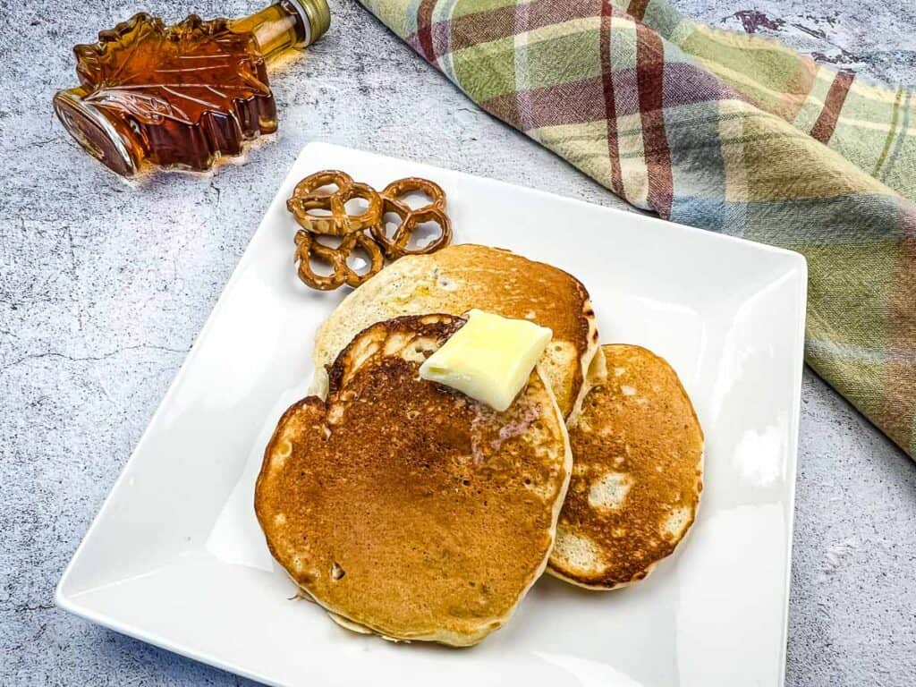A horizontal shot of Pretzel Pancakes on a plate with butter and syrup in the background.