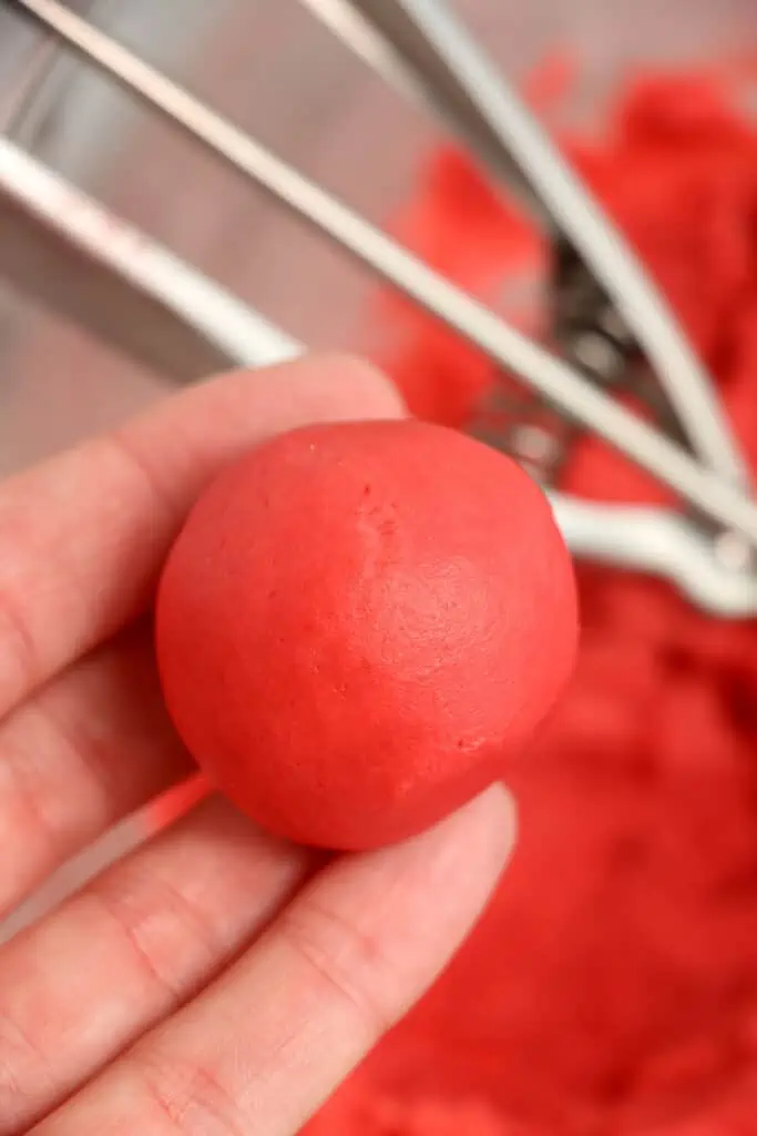 A hand holding a ball of rolled red velvet cookie dough.