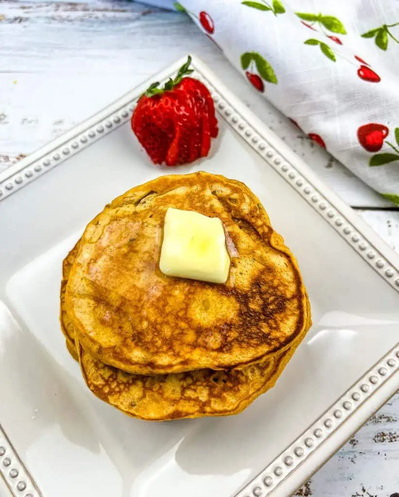A stack of Sweet Potato Pancakes with pecans on a plate with a strawberry in the background.