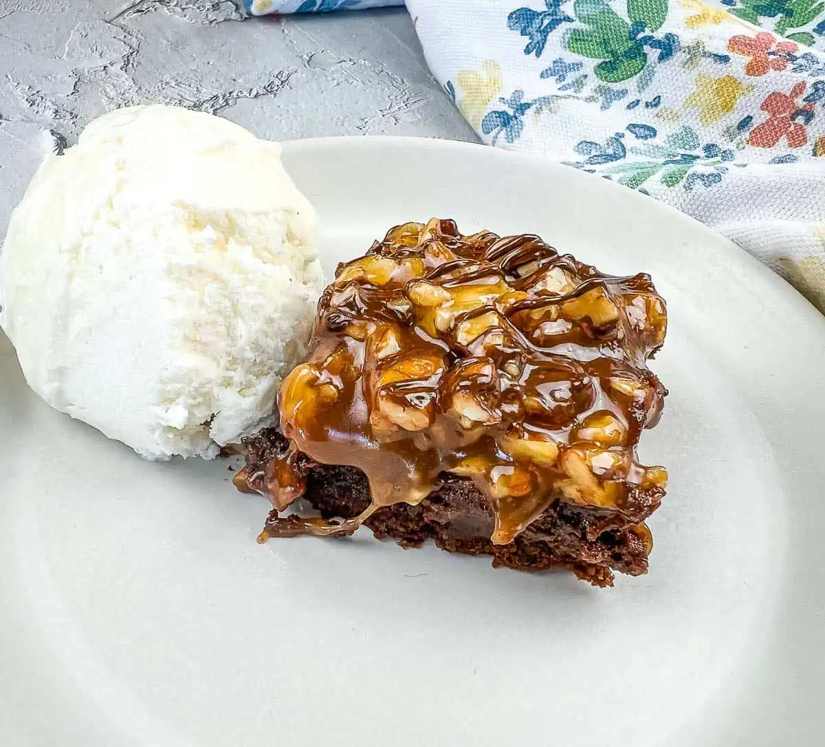 A piece of Turtle Brownie with ice cream on a plate.