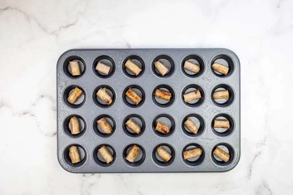 A piece of sausage in the bottom of each cup of a muffin tin.