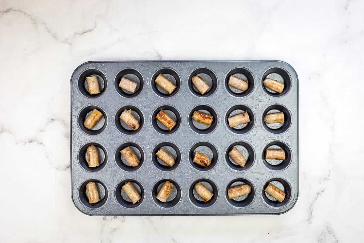 A piece of sausage in the bottom of each cup of a muffin tin.