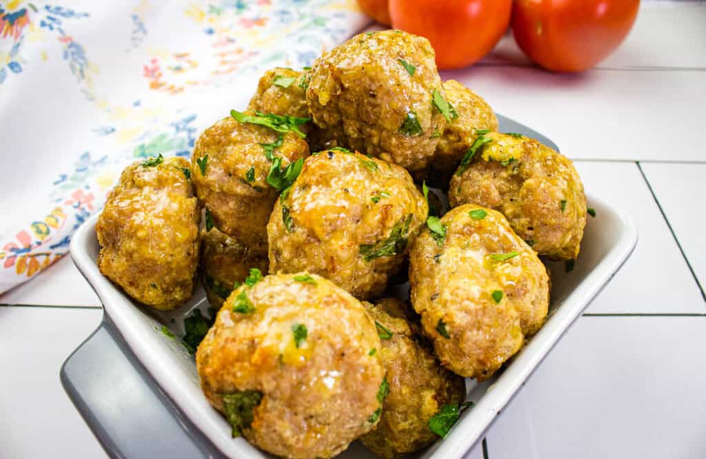 Meatballs in a white bowl with herbs.