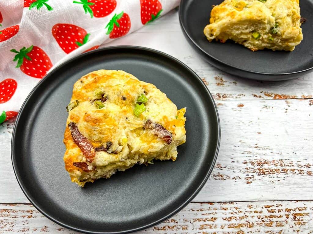 A top-down shot of 2 bacon cheddar green onion scones on black plates.