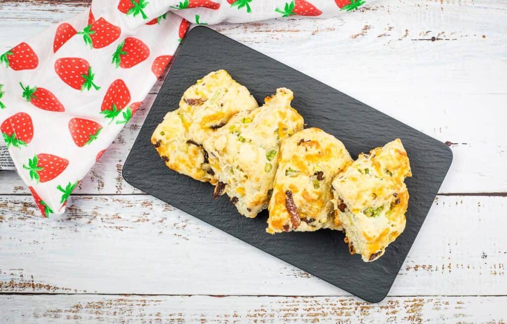 A top-down horizontal shot of Bacon, Cheddar, Green Onion Scones on a black platter.