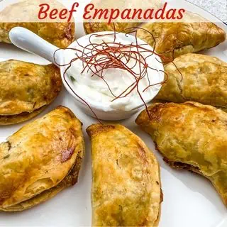 Air fryer beef empanadas on a plate with sour cream in the middle.