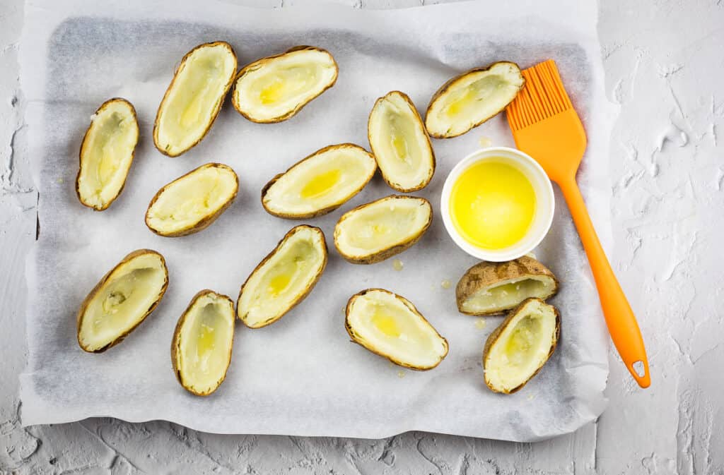 Potato skins on a baking sheet brushed with butter.