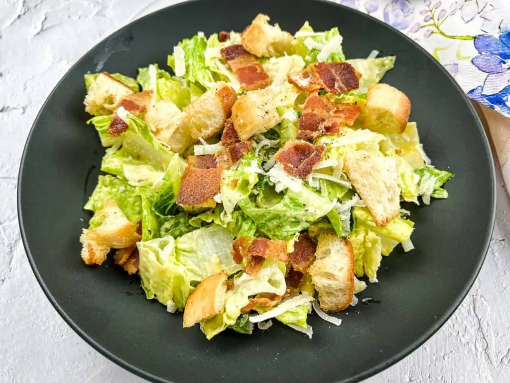 Caesar salad with bacon croutons in a black bowl.