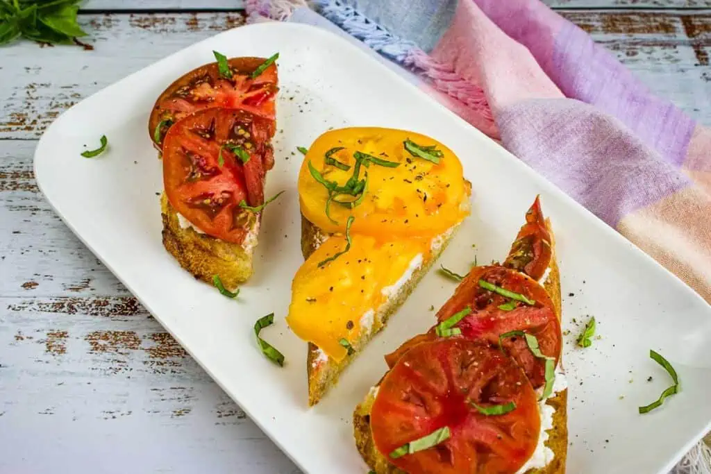 Three slices of grilled bread with tomatoes and ricotta on a plate.