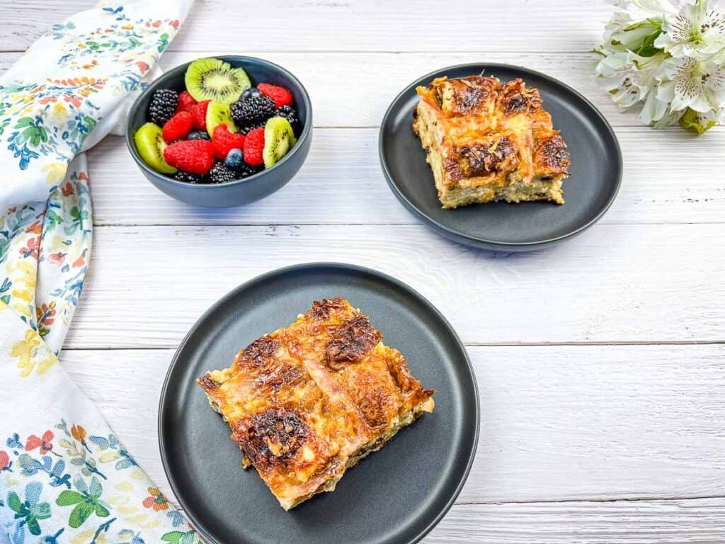 A horizontal image of 2 servings of hot cross bun brunch casserole on black plates.