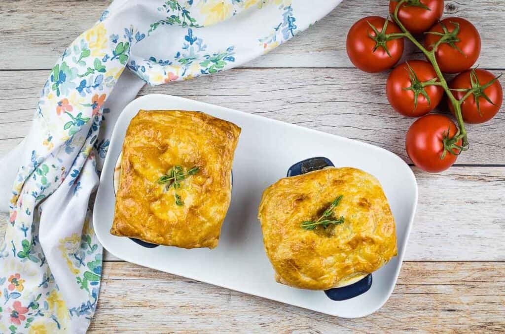 2 Leftover Roast Beef Pot Pies on a table with tomatoes in the background.