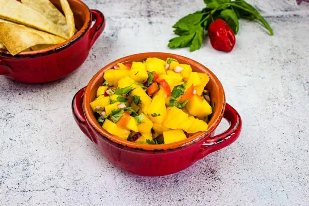 Two bowls of mango salsa with tortilla chips.