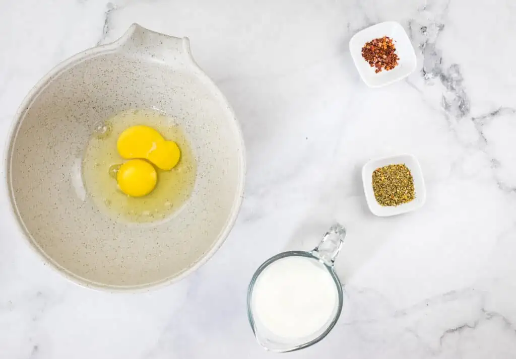 Cracked eggs in a bowl next to milk and spices.