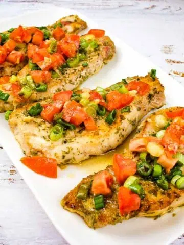Three pork chops with tomatoes and green peppers on a white plate.