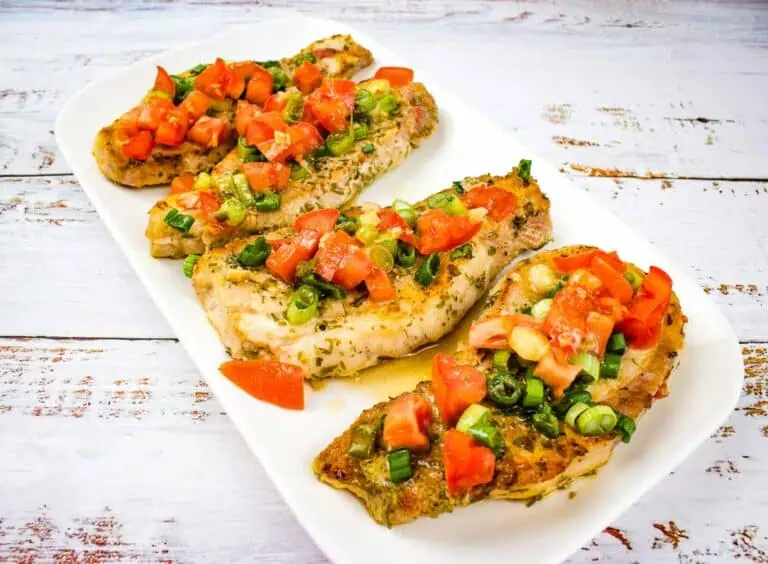 Three pork chops with tomatoes and green peppers on a white plate.