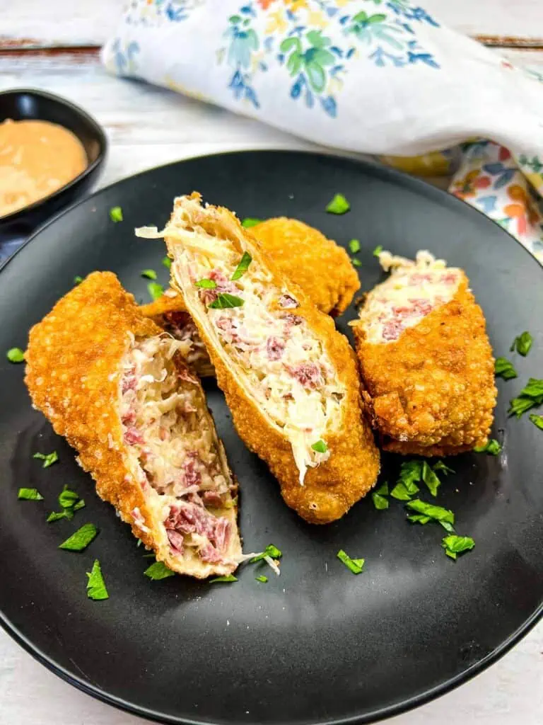 Reuben Egg Rolls cut in half on a black plate.