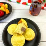 Pancake bites with sausage on a black plate with fruit and syrup in background.