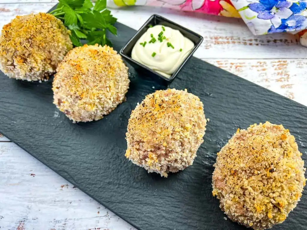 Finished Scotch Eggs on a black platter.