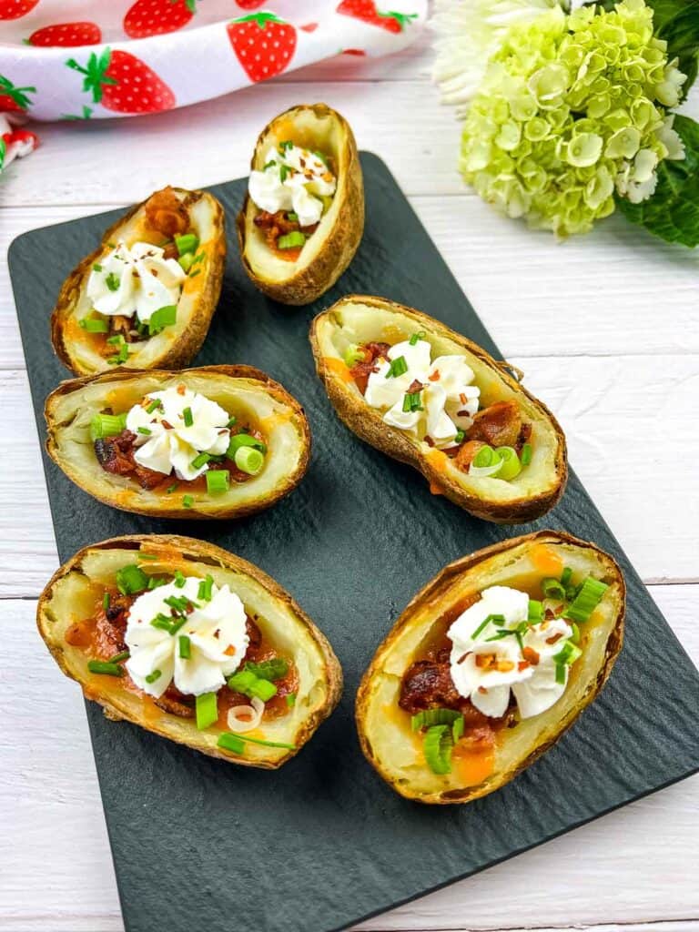 Fully loaded Baked Potato Skins on a black platter.