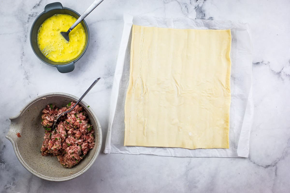 Mixed filling next to a bowl of egg wash and puff pastry.