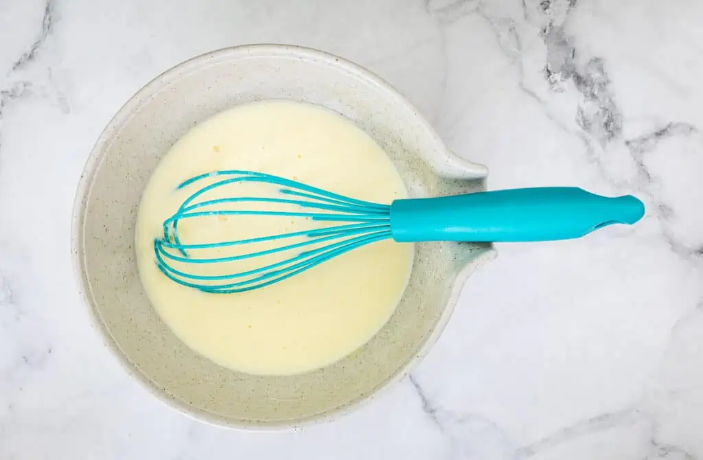 Mixed wet ingredients in a bowl with a whisk.