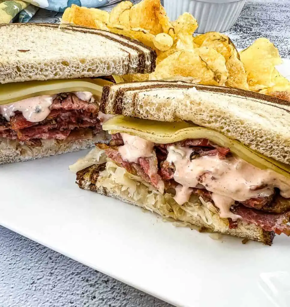 A cut Pastrami Reuben Sandwich on a plate with chips.