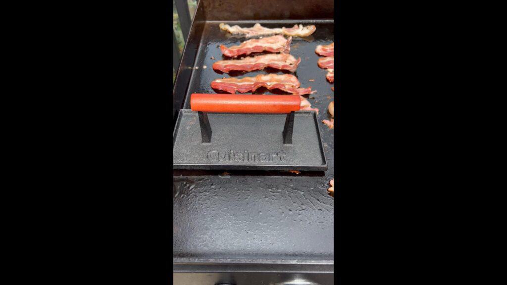 A bacon press on the bacon.