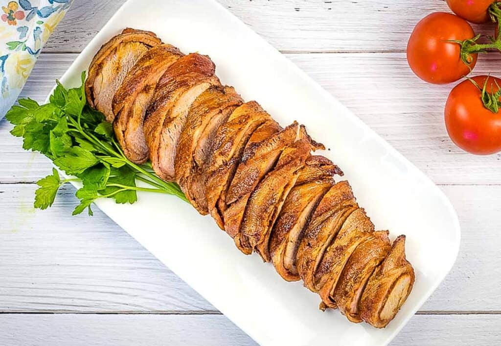 Sliced bacon wrapped pork on a white platter.