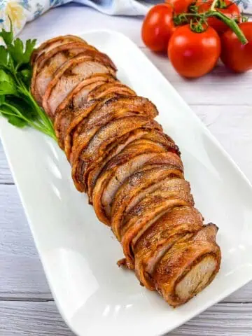 Smoked bacon-wrapped whole pork tenderloin sliced on a plate.