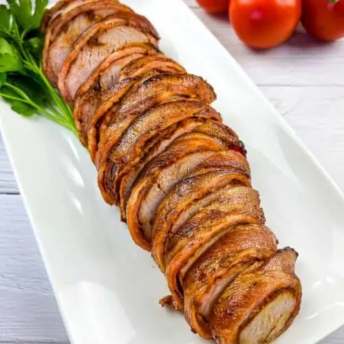Smoked bacon-wrapped whole pork tenderloin sliced on a plate.