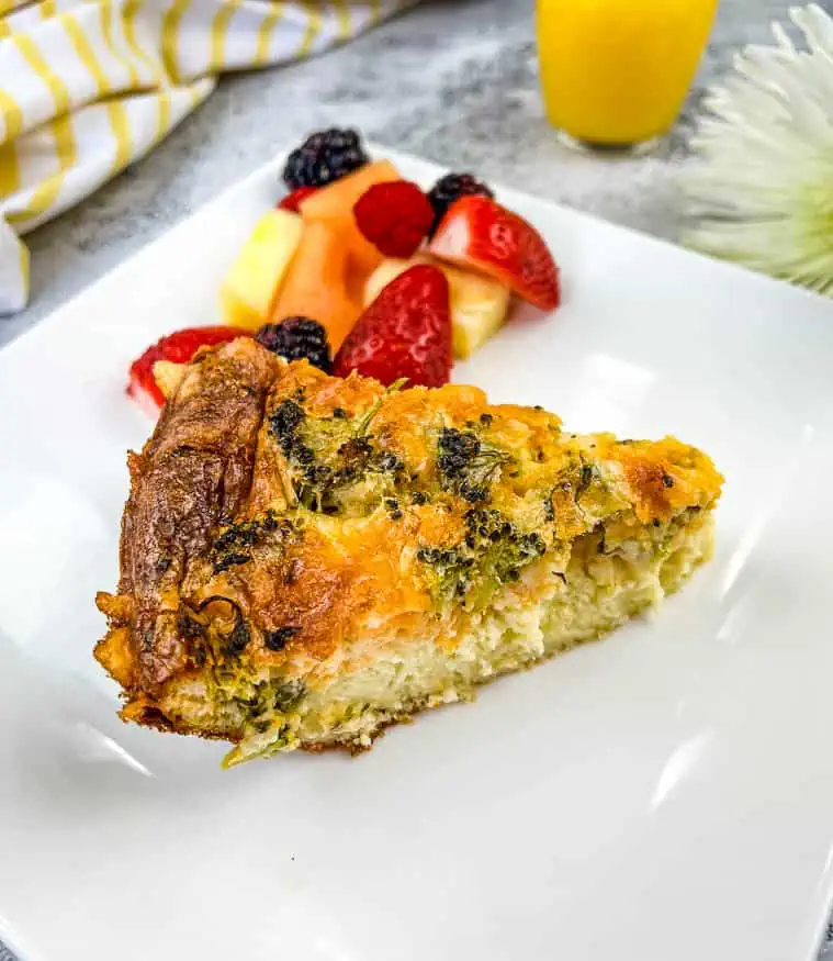 A slice of ham and cheese impossible quiche on a plate with fruit.