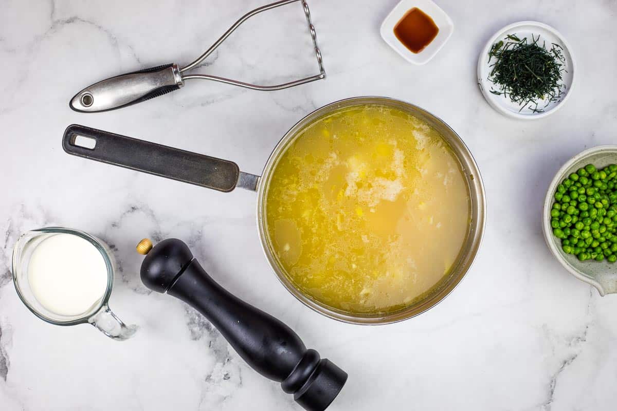Soup with some partially mashed potatoes in it with remaining ingredients nearby.