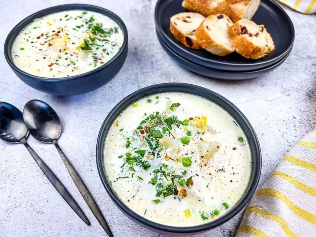 Two bowls of Potato & Pea Chowder in black bowls with bread in the background.