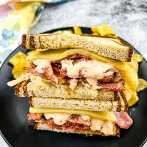 A stacked Pastrami Reuben Sandwich on a black plate.