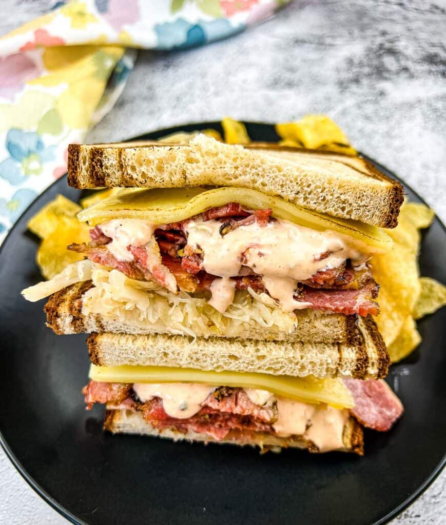 A stacked Pastrami Reuben Sandwich on a black plate.