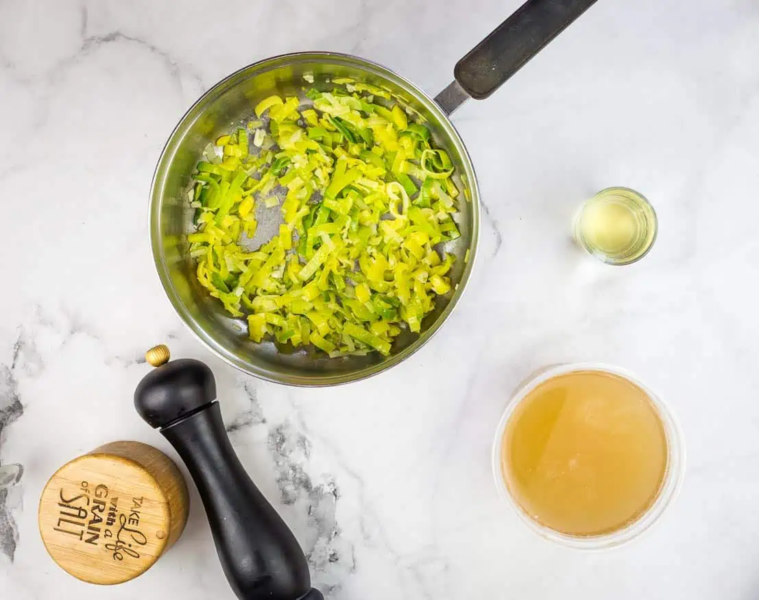 Leeks in a soup pot with ingredients nearby.