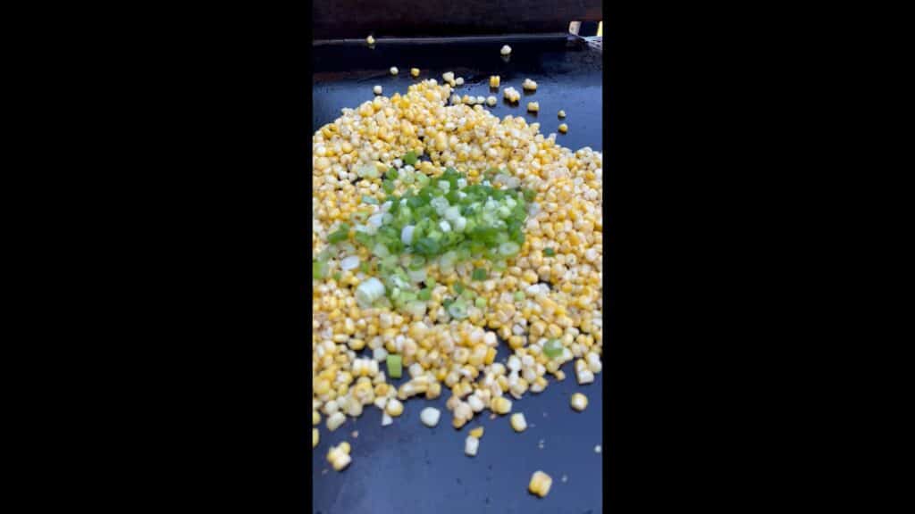 Green onions and garlic added to corn on the griddle.