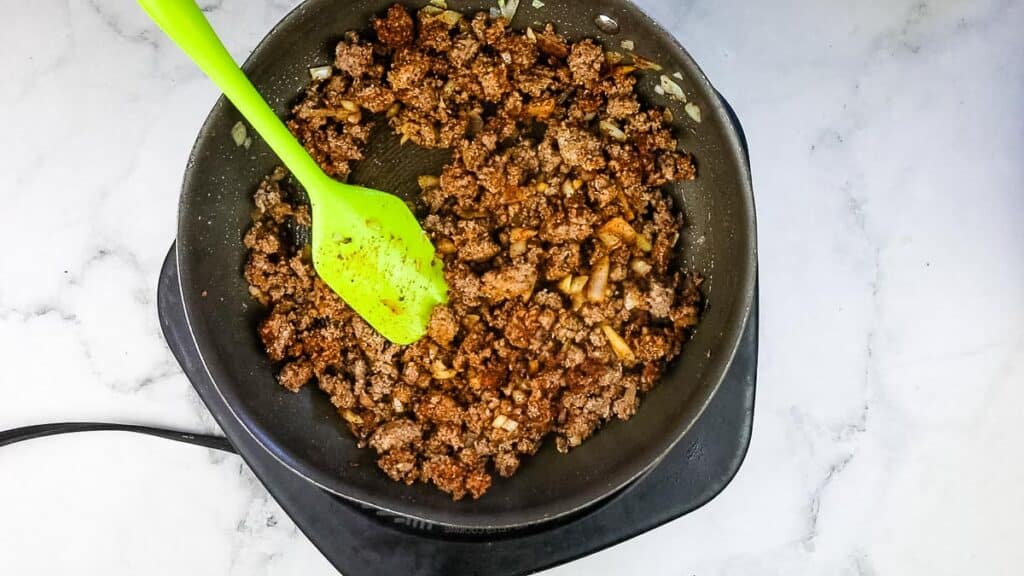 Ground beef, onions, and seasoning mixed in a skillet.