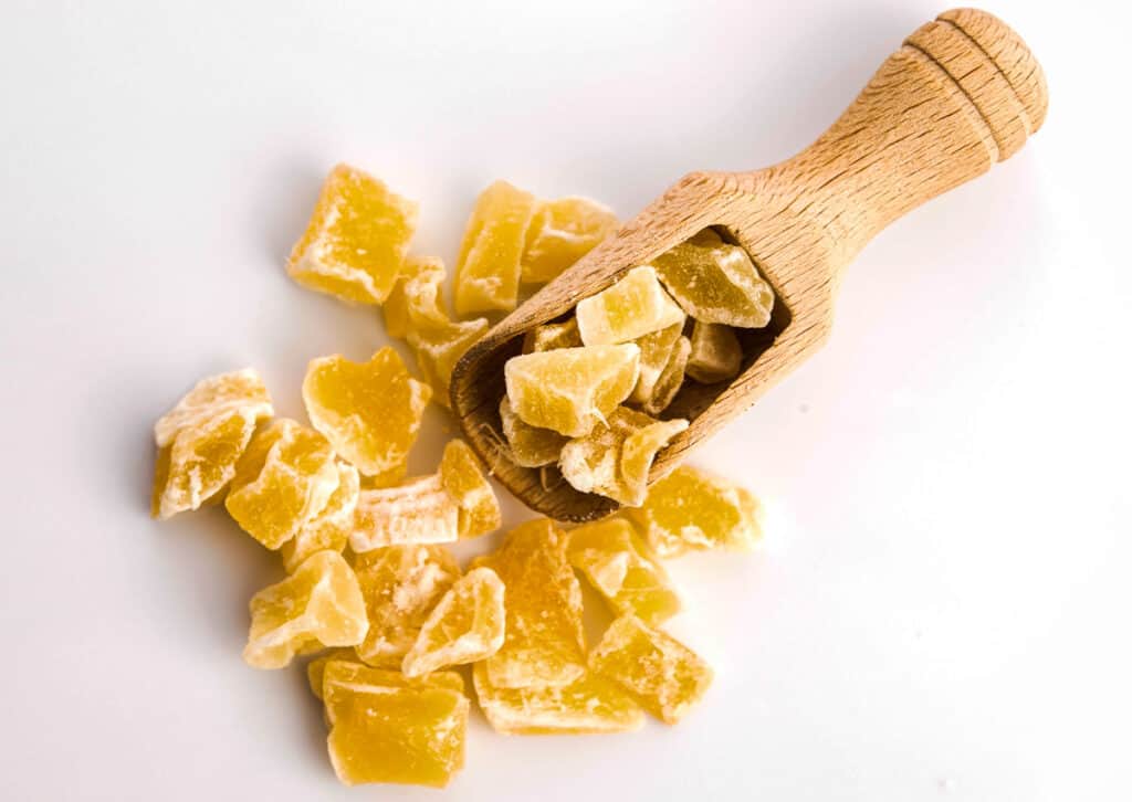 Candied ginger on a white background with wooden scoop.