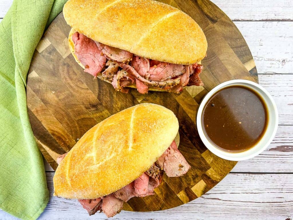 A top down shot of 2 Smoked French Dip sandwiches on a board with jus.