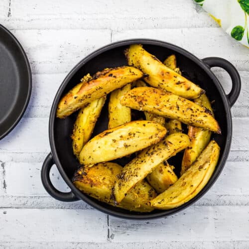 A top-down shot of Greek Lemon Potatoes in a black bowl.