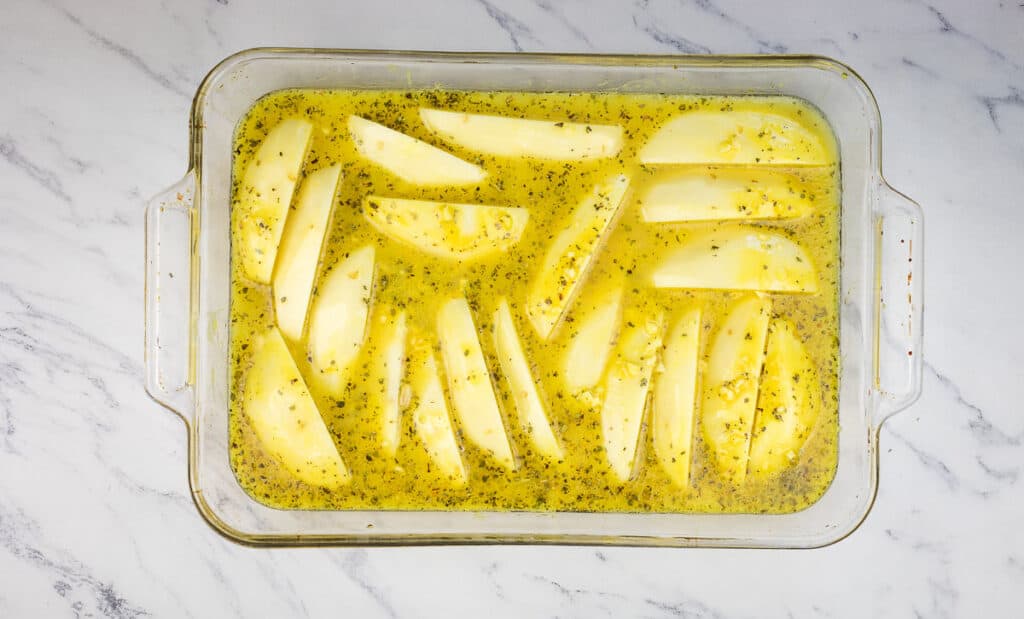 Potatoes in a baking dish with chicken broth.