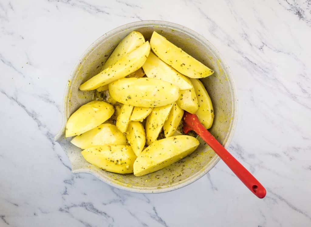 Potatoes tossed with dressing in a bowl.