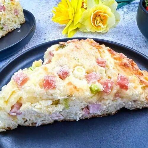A Ham & Cheese Scone on a black plate with flowers in the background.