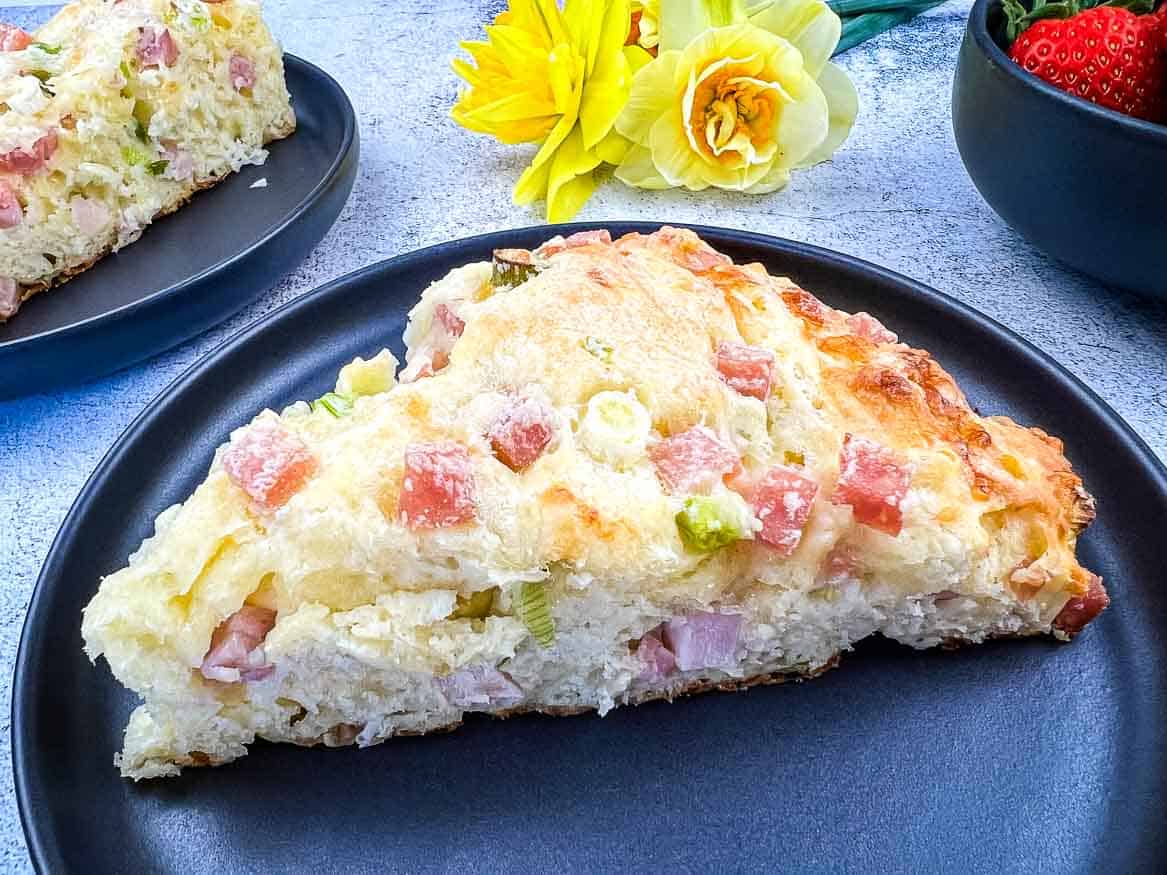 A Ham & Cheese Scone on a black plate with flowers in the background.