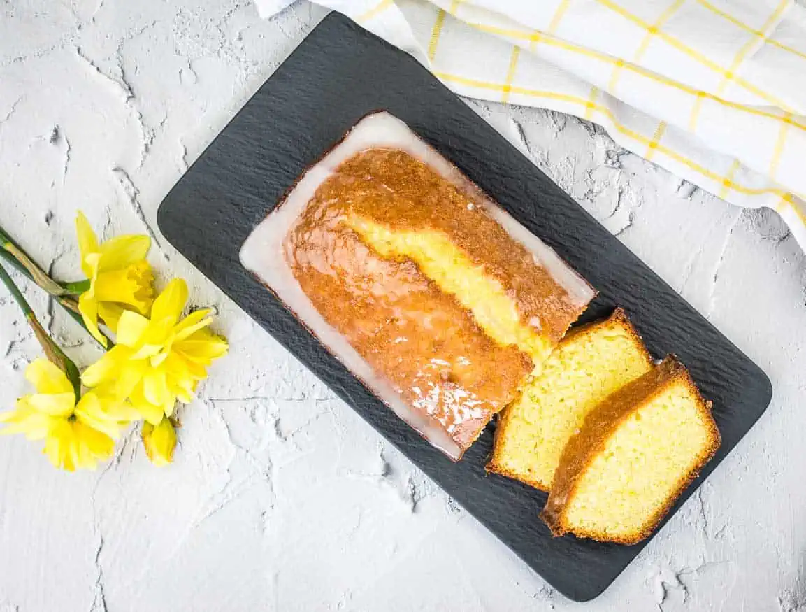 A slice of lemon pound loaf on a plate with daffodils.