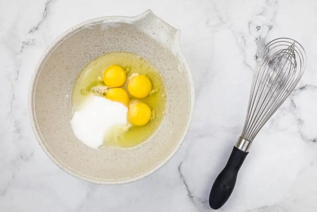 Sugar, eggs, and salt in a bowl with a whisk nearby.