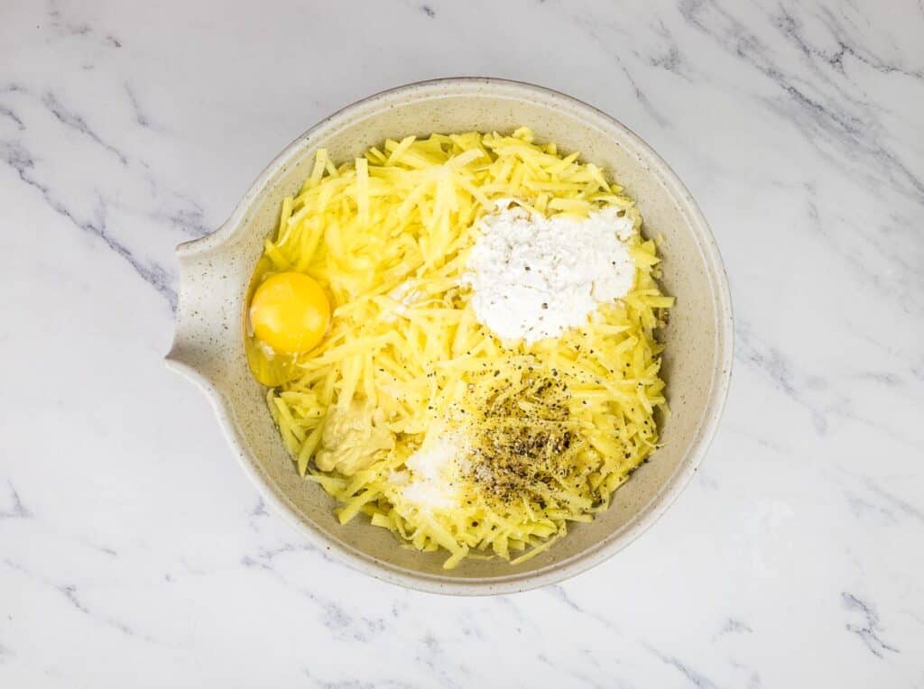 Shredded potatoes, egg, flour, and dijon mustard in a bowl.
