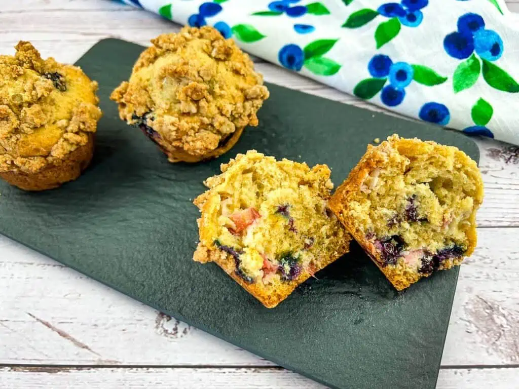 A horizontal image of blueberry-rhubarb muffins with one cut in half.